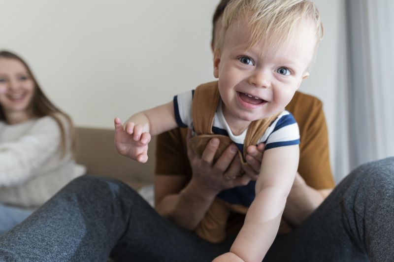 Ein fröhliches Kind wird von seinen Eltern gehalten, während es in die Kamera lacht.