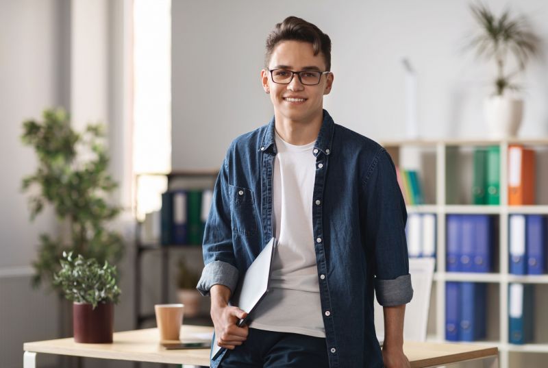 Ein junger Unternehmer steht mit einem Laptop in einem modernen Büro, als er über Wohnungen in Magdeburg nachdenkt.