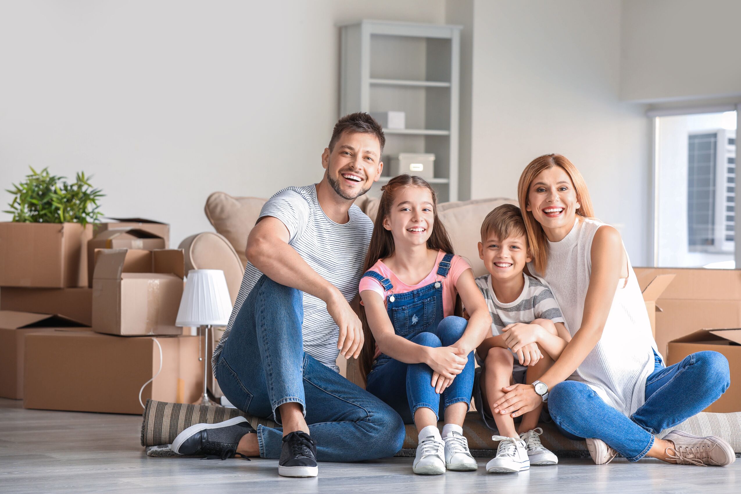 Eine glückliche Familie sitzt umgeben von Umzugskartons in ihrer neuen Wohnung in Magdeburg.