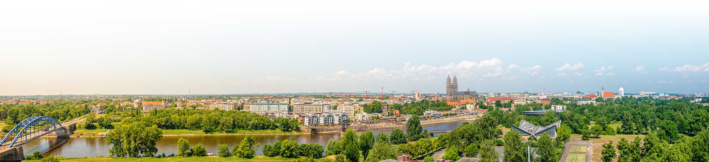 Panoramablick auf Magdeburg mit Fluss und Brücke unter klarem Himmel.